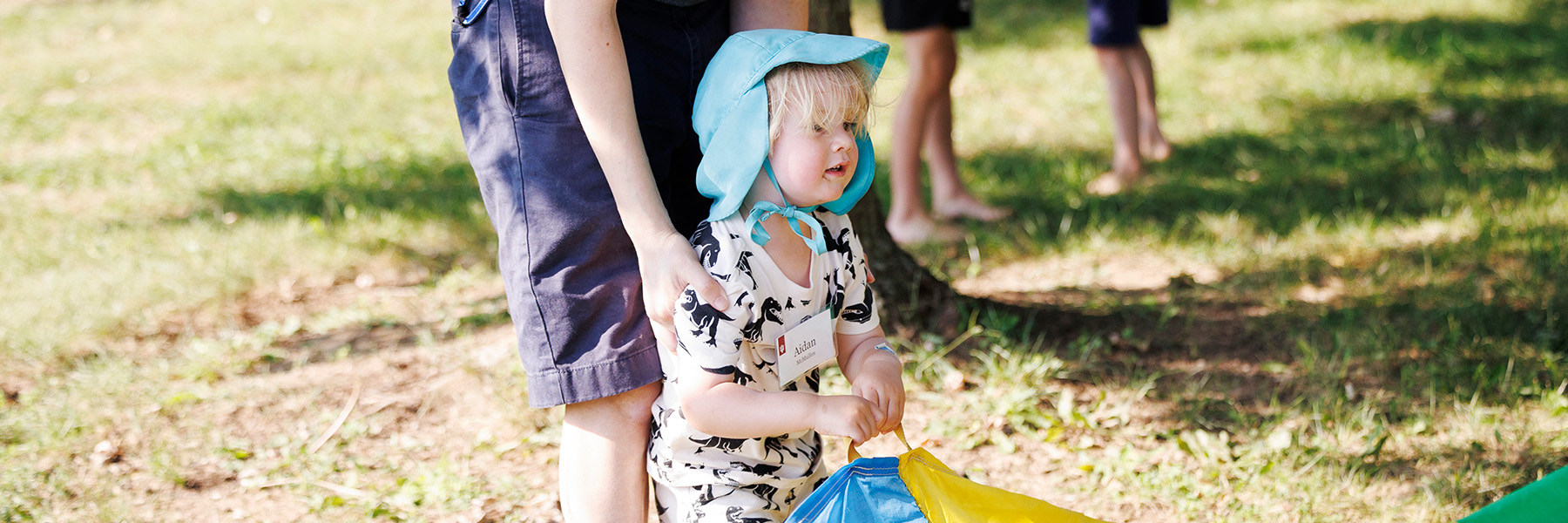 An adult helps a toddler participate in a parachute game