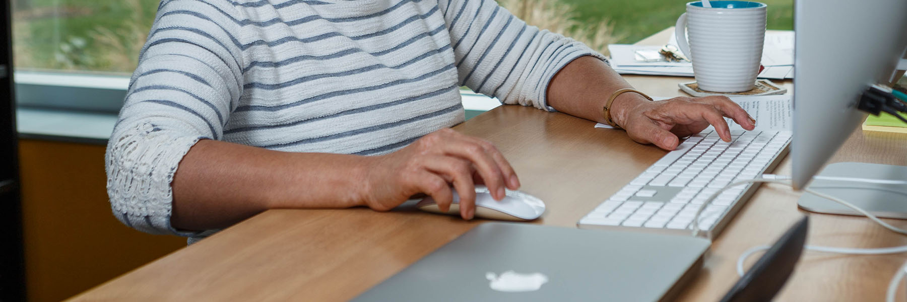 A closeup view of a woman's arms using a keyboard and mouse